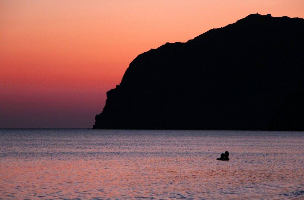 silhouette of 2 people sitting on rock formation during sunset