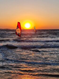 Two windsurfers ride the waves under a stunning sunset in Rhodes, Greece.